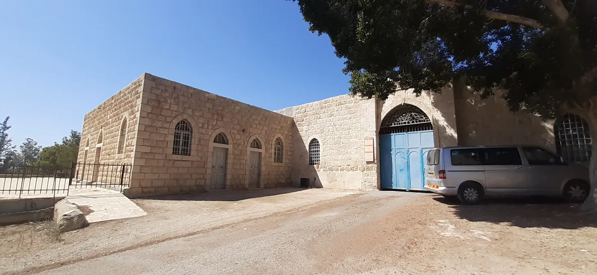 Stone buildings and blue gate of the Beit Jamal monastery under a large tree
