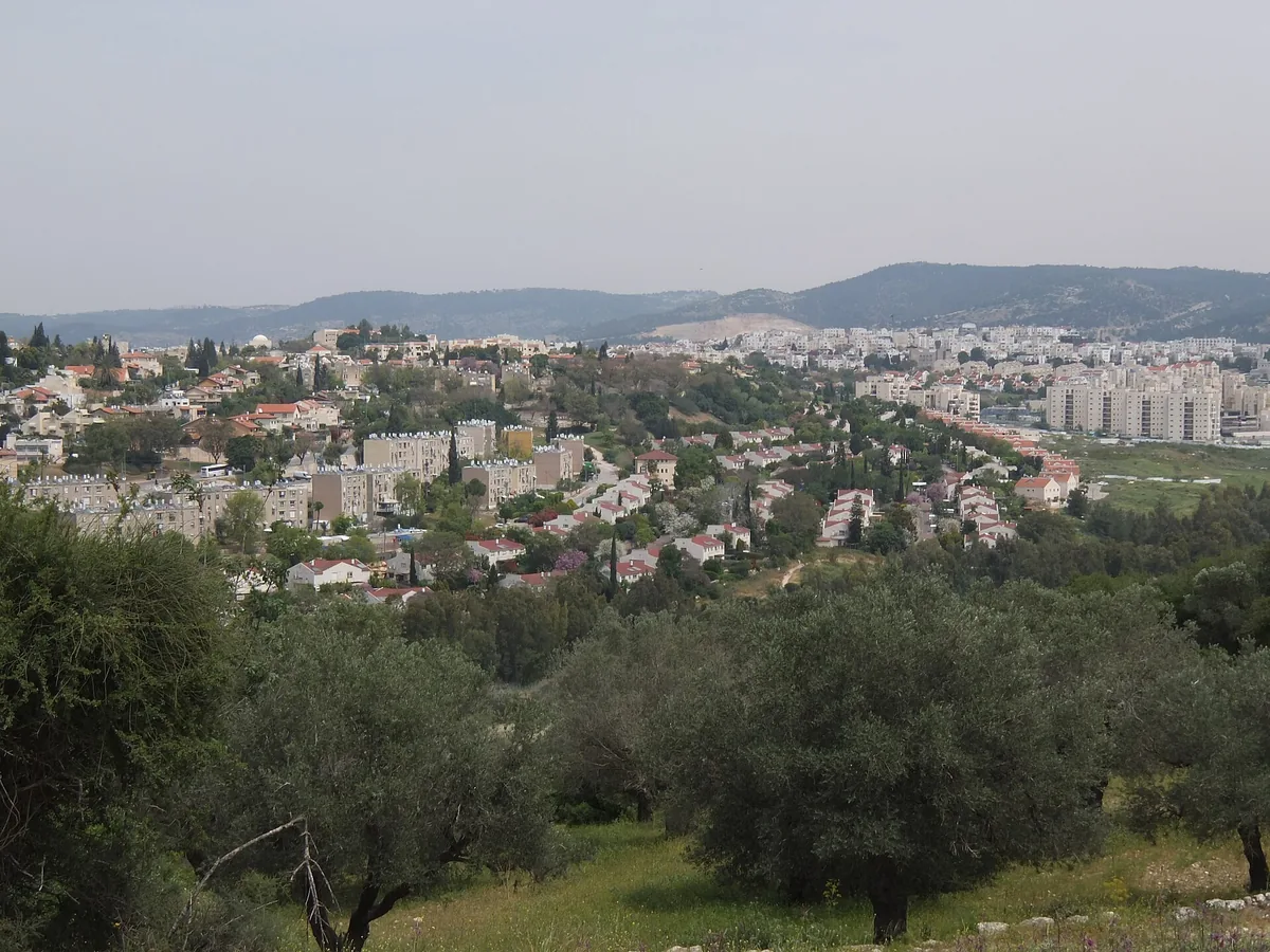 Beit Shemesh seen from the southwest across olive trees, with red-roofed houses and apartment blocks below the Judean hills