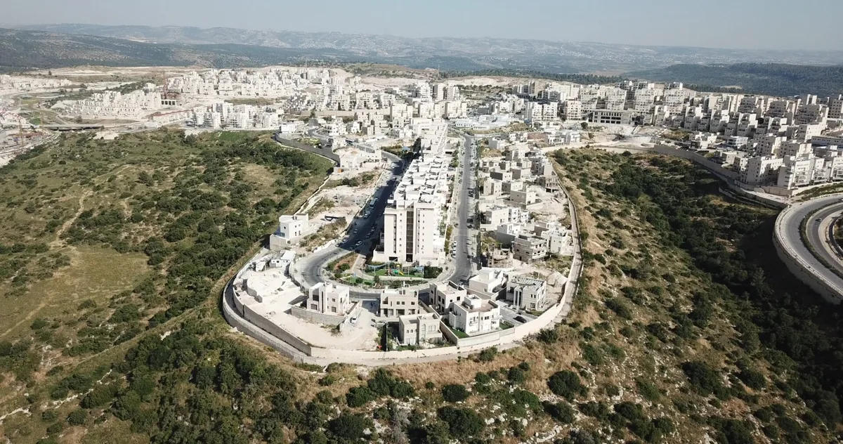 Aerial view of Ramat Beit Shemesh Gimmel: pale stone apartment blocks along a ridge, with wooded hills around
