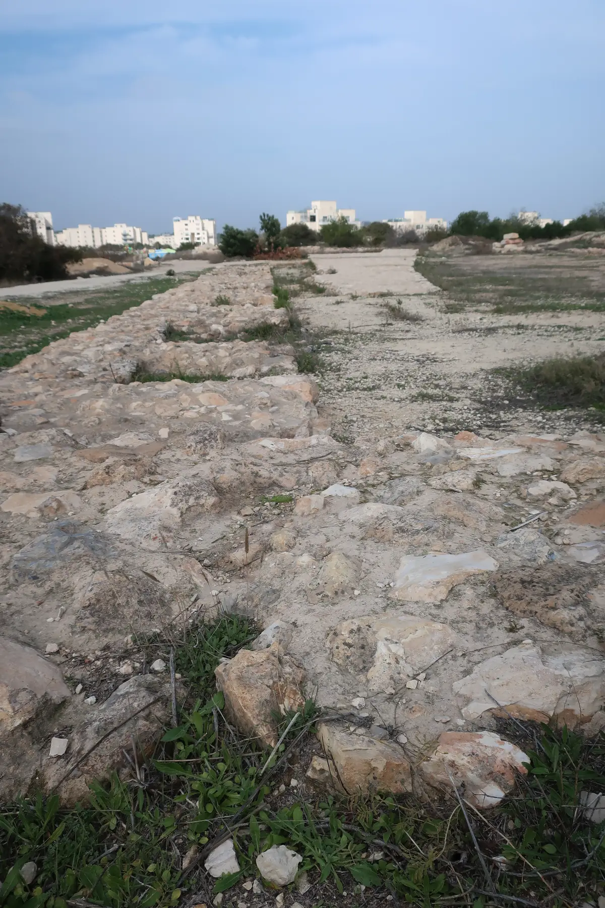 Excavated stone wall foundations at Tel Yarmut, with new Ramat Beit Shemesh apartment blocks in the distance